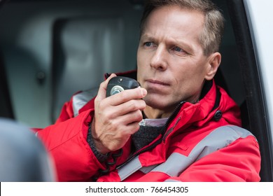handsome middle aged male paramedic talking by portable radio while sitting in ambulance
