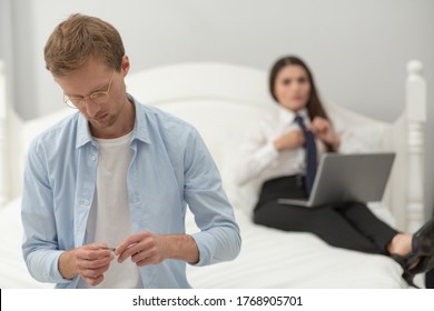 Handsome Middle Aged Man Polishing His Nails. Man Wearing All White Outfit And Thin Round Glasses Polishes His Nails While His Wife Is Working With Laptop In Background.