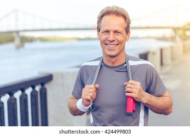 Handsome Middle Aged Man In Sports Uniform Is Warming Up, Holding A Jumping Rope And Smiling During Morning Run