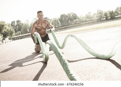 Handsome middle aged man working out on a running track. Healthy adult man doing battle rope exercise. Tanned skin and shirtless middle-aged man. - Powered by Shutterstock