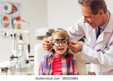 Handsome middle aged ophthalmologist examining little boy with modern equipment, both smiling