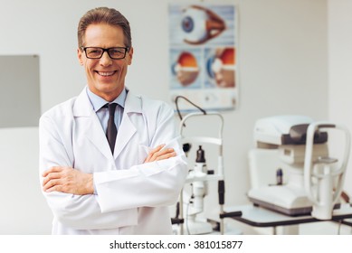 Handsome middle aged ophthalmologist looking at camera and smiling while standing in his office - Powered by Shutterstock