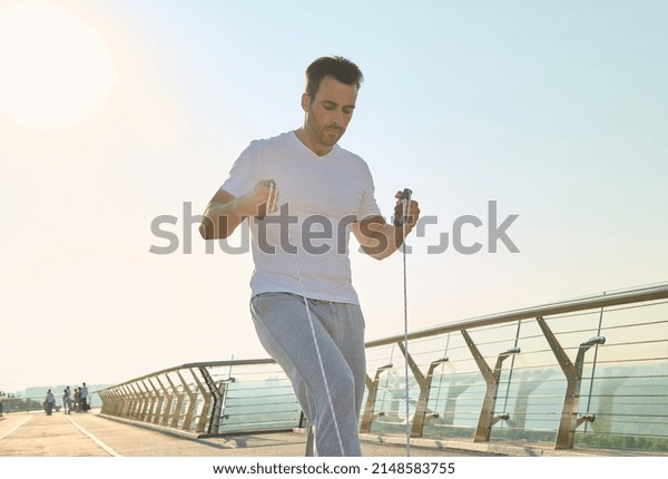 Handsome middle aged sportsman, muscular build
Caucasian middle aged man training with jumping rope on a city
bridge treadmill early in the morning on a beautiful sunny summer
day. Keep your body
fit