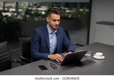 Handsome middle eastern entrepreneur working at modern office, arabic businessman sitting at workdesk, typing on laptop keyboard, drinking coffee, sending emails, copy space, high angle view - Powered by Shutterstock