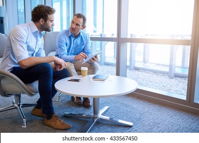Handsome middle-aged business executive sitting with a younger coworker in a bright modern office, explaining some information to him on a digital tablet - Shutterstock ID 433567450