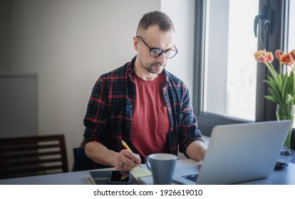 Schöner Mann mittleren Alters in Gläsern, die zu Hause arbeiten und den Bildschirm des Laptops sehen. Remote-Mitarbeiterkonzept...