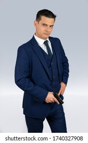 Handsome Middle-aged Man Posing In A Fancy Blue Suit Holding A Small Gun And Gray Background