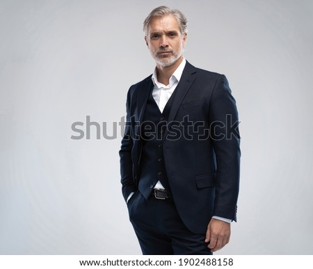Handsome middle-aged man in suit posing against grey background