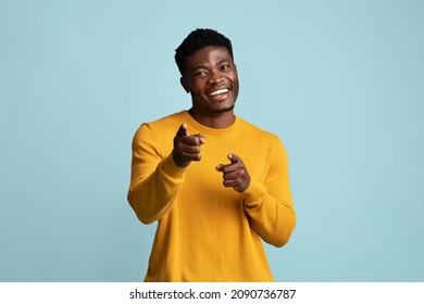 Handsome millennial black guy in yellow posing on blue studio background, cheerfully smiling and gesturing at camera, african american young man showing index fingers, flirting, copy space