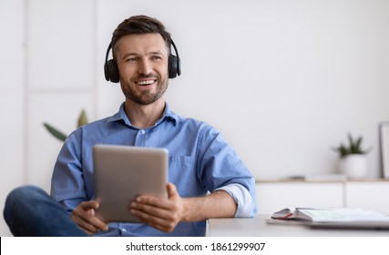 Handsome Millennial Freelancer Guy In Wireless Headphones Relaxing With Digital Tablet At Home Office, Having Break In Work, Sitting At Desk With Notepad, Listening Music And Looking Away, Copy Space - Powered by Shutterstock