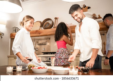 Handsome Millennials Friends Group Bonding At Home Preparing Snacks For Aperitif - Two Heterosexual Couple Having Fun Together In The Kitchen Cooking For Dinner - Focus On Bearded Man With White Shirt