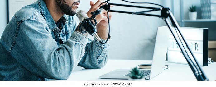 Handsome Mixed race content creator streaming his show at home studio using professional microphone and laptop, wide screen