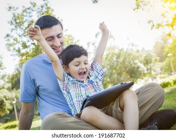 Handsome Mixed Race Father And Son Playing On A Computer Tablet Outside.