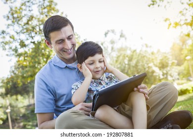 Handsome Mixed Race Father And Son Playing On A Computer Tablet Outside.