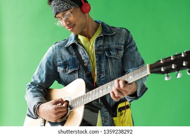 handsome mixed race man in denim and headphones playing acoustic guitar on green screen - Powered by Shutterstock