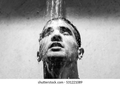 Handsome model faceshot with his head under the pooring water from the shower, in black & white
