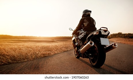 Handsome motorcyclist in leather jacket and helmet at sunset on the road in warm sun rays - Powered by Shutterstock