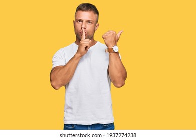 Handsome muscle man wearing casual white tshirt asking to be quiet with finger on lips pointing with hand to the side. silence and secret concept. 
