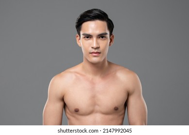 Handsome muscular Asian man with black hair and naked torso on gray isolated background in light studio