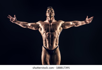 Handsome muscular bodybuilder posing over black background. Glory of the champion.