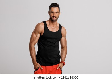 Handsome muscular man in black tank top posing on gray background 