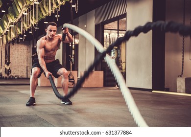 Handsome muscular man is doing battle rope exercise while working out in gym