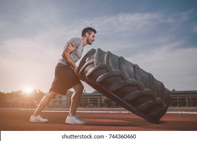 Handsome muscular man flipping big tire outdoor. - Powered by Shutterstock