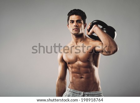 Handsome muscular man holding kettle bell with copy space. Hispanic male athlete working out with kettlebell on grey background. Crossfit workout theme.