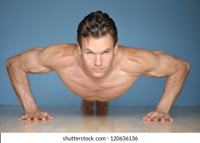 Handsome Muscular Man Looks At Camera While Performing Pushup On Floor With Blue Wall Background