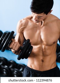 Handsome muscular man with nude body uses his dumbbell to exercise flexing bicep muscle