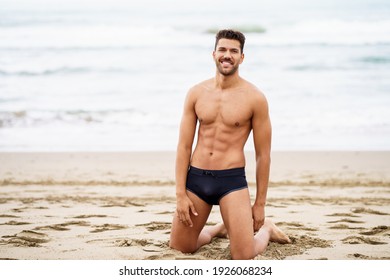 Schöner, muskulöser Mann auf den Knien auf dem Sand des Strandes