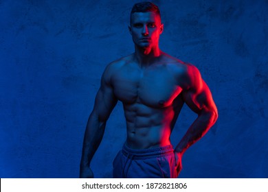 Handsome muscular man posing in the colorful light