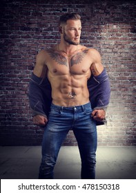 Handsome muscular man with sweater open on naked torso, standing, in studio shot