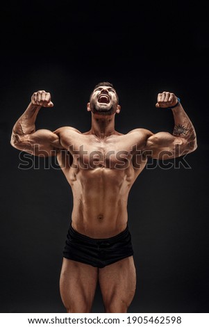 Handsome muscular shirtless man screaming and looking up isolated on black.