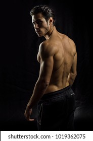 Handsome muscular shirtless young man standing confident, profile view, looking at camera