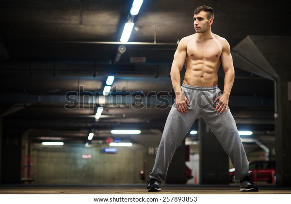 Handsome muscular young man posing at parking\
garage, natural lights, dark\
place.