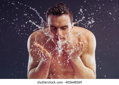 Handsome naked man is washing up, splash of water, on a dark background