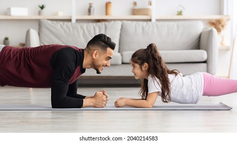 Handsome Niddle-eastern Man Loving Father And Cute Little Girl Daughter In Sportswear Planking Together At Home, Standing Face To Face And Smiling, Side View, Panorama With Copy Space