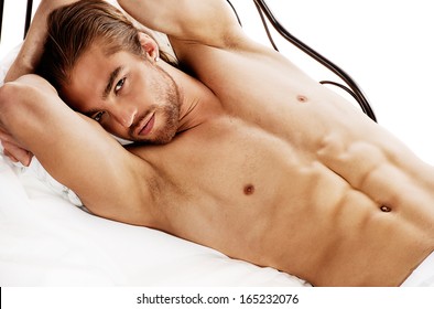 Handsome nude man lying in a bed. Isolated over white.