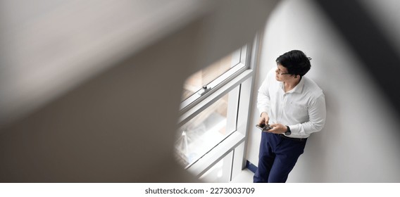 Handsome office worker hold mobile phone in hand chat with girlfriend by mobile phone looking out through window at modren office balcony in relax time.
