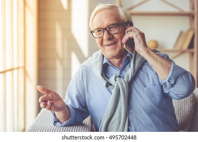 Handsome Old Man Dressed In Smart Casual Style And Eyeglasses Is Talking On The Mobile Phone And Smiling While Sitting On Couch At Home