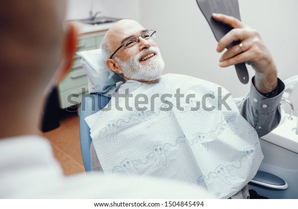 Handsome\
old man talking to the dendist. Two men in the dentist\'s office.\
Grandfather looking into the mirror on his\
teeth