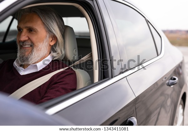 Handsome older gentleman is enjoying his drive in his\
new car
