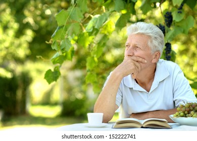 Handsome Older Man Sitting At A Table At Home On The Veranda