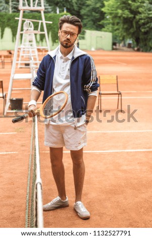 handsome old-fashioned tennis player with racket on brown court near tennis net