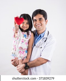 Handsome Paediatric Male Doctor Holding A Baby Girl Patient Holding Red Stuffed Heart Toy, Isolated Over White Background