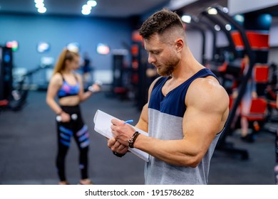 Handsome personal trainer with a clipboard in fitness center. Fitness instructor takes notes. Closeup. - Powered by Shutterstock