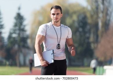 Handsome Personal Trainer With Stopwatch Showing Thumbs Up Sign in City Park Area - Training and Exercising for Endurance - Healthy Lifestyle Concept Outdoor - Powered by Shutterstock