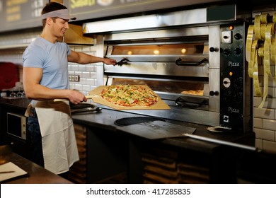 Handsome pizzaiolo making pizza at kitchen in pizzeria. - Powered by Shutterstock