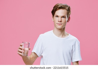 a handsome, pleasant red-haired guy in a white T-shirt, symbolizing purity, with a glass glass of water in his hands and looks kindly into the camera. Balance and replenishment of fluids in the body - Shutterstock ID 2211615515